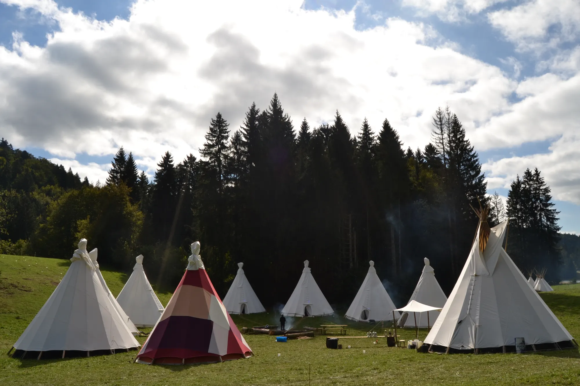 Camp d’une vingtaine de tipis écrus alignés dans une clairière