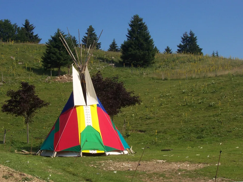 Tipi peint de bandes rouges, jaunes et vertes dans un pré en pente