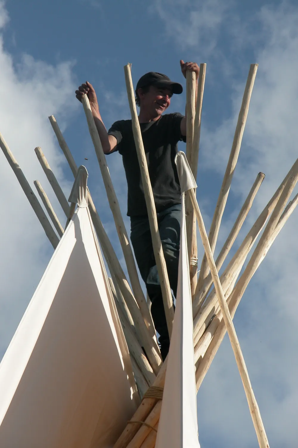 Membre de l’atelier debout parmi les perches d’un tipi en montage