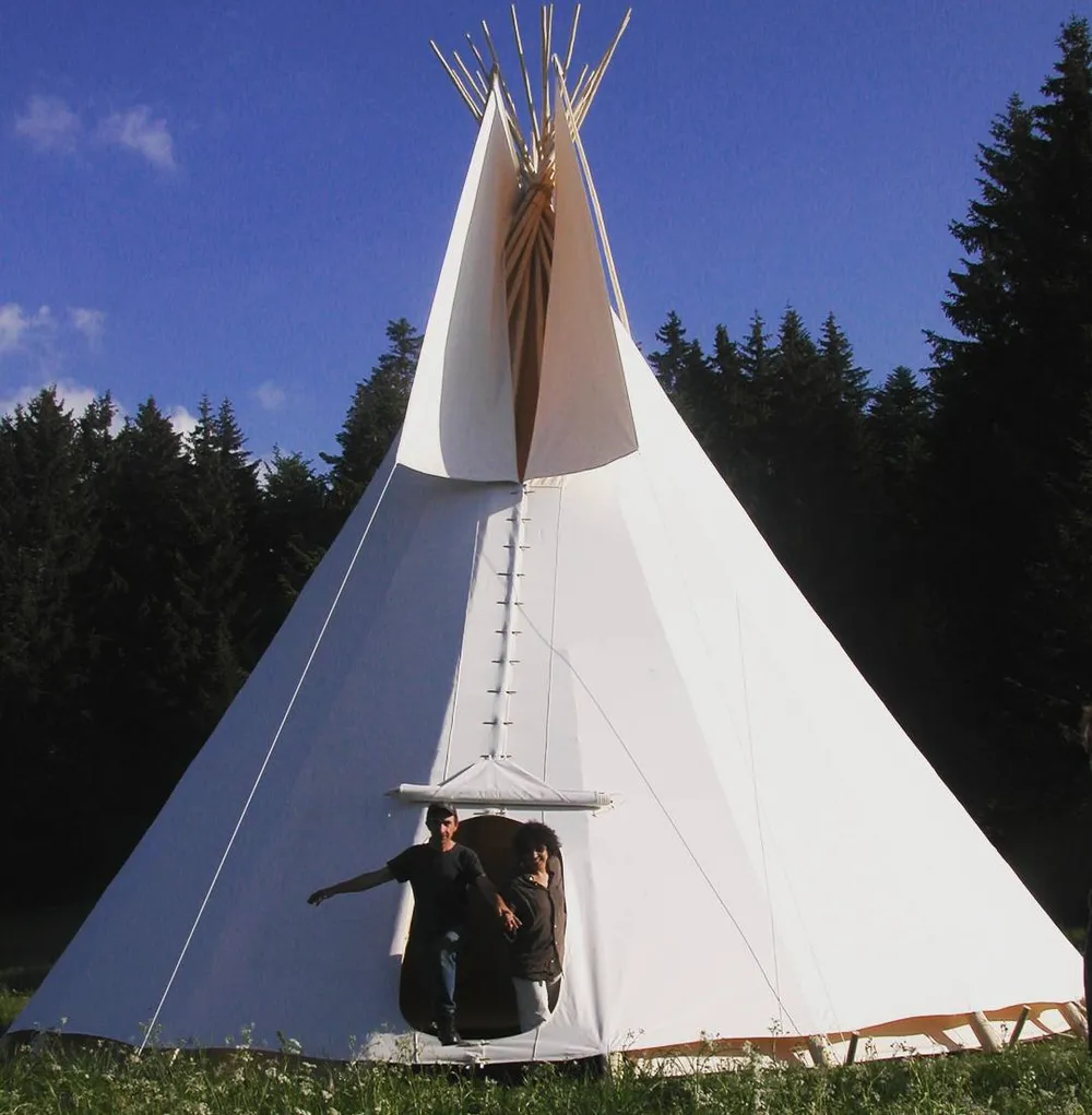 Deux personnes debout dans l’ouverture d’un grand tipi, qui donne l’échelle