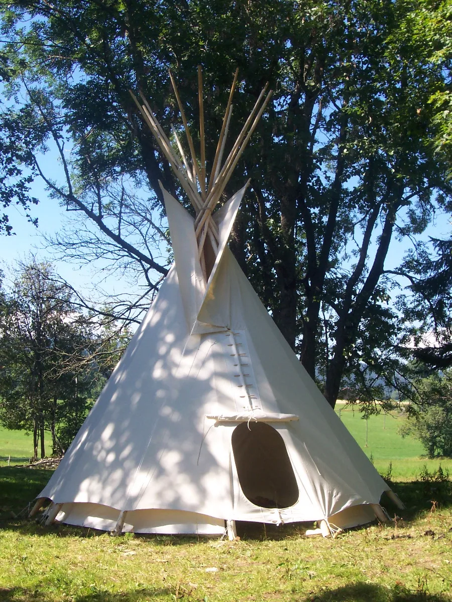 Tipi écru dressé dans un pré ensoleillé, porte ouverte
