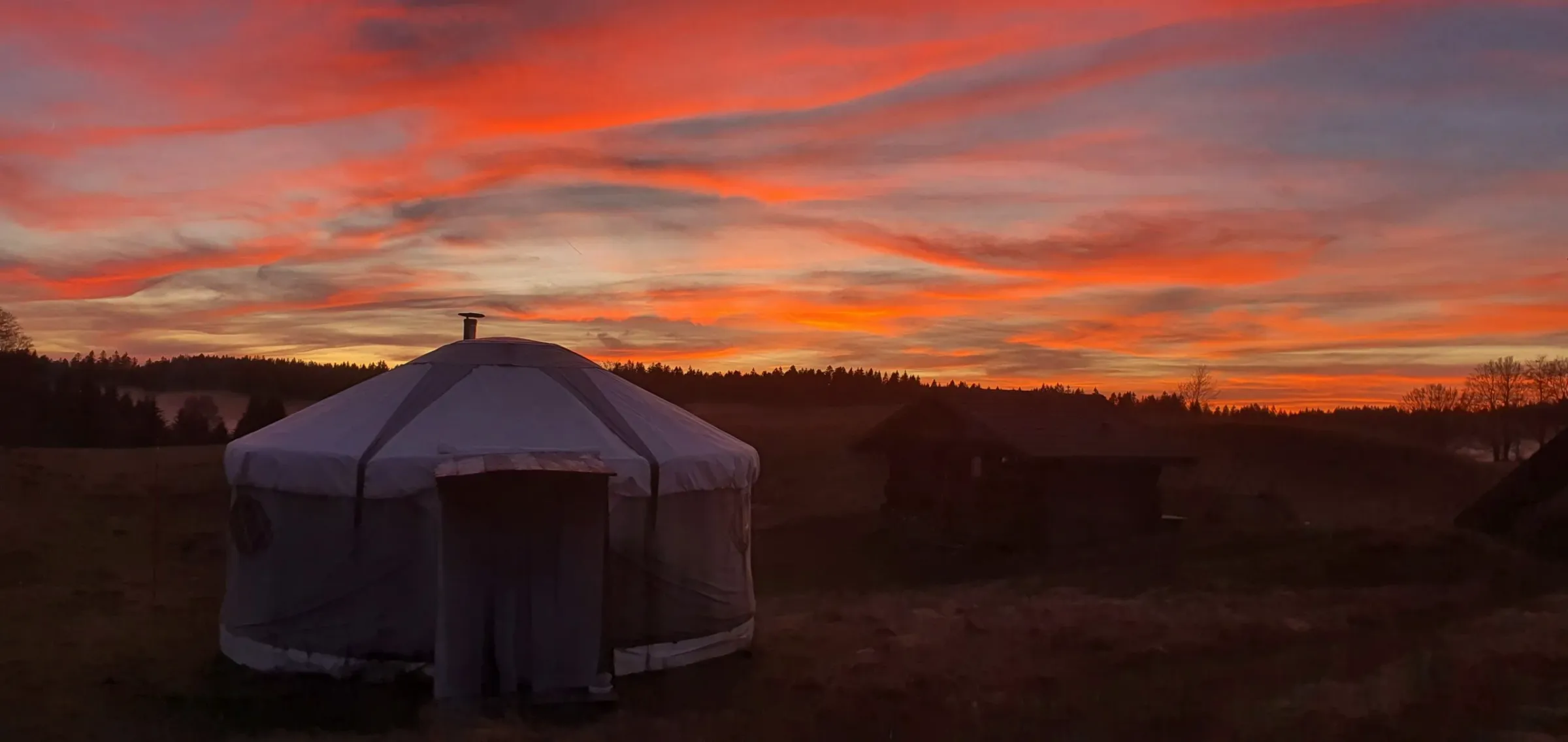 Yourte écrue dans un pré, sous un ciel de coucher de soleil embrasé